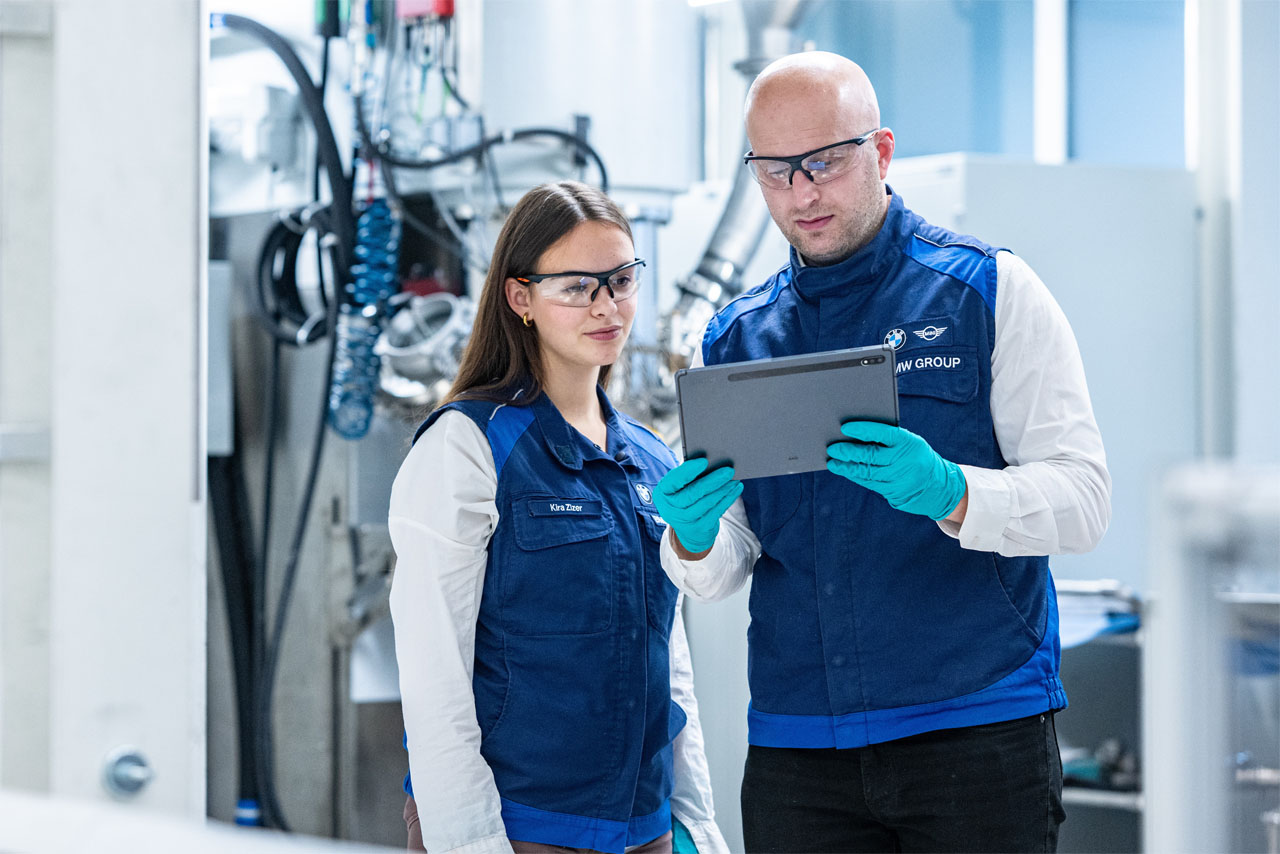 Two BMW Group employees analyse AI-supported data from battery cell production on a tablet.