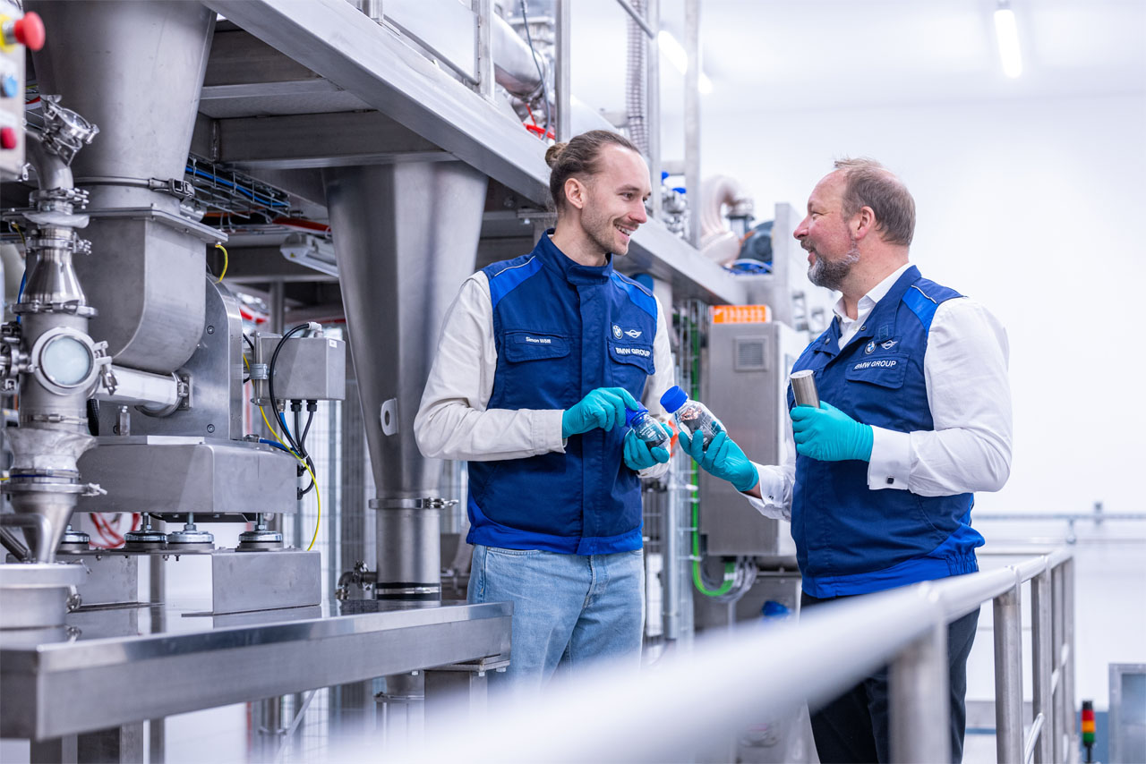 Two experts examine recycled battery material samples beside an electrode recycling system in the BMW Group Cell Recycling Competence Centre (CRCC) in Salching, Lower Bavaria.